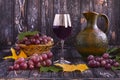 Glass of red wine, ripe grapes in straw basket, wine jug on dark wooden background. Autumn composition Royalty Free Stock Photo