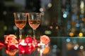 Glass red wine, roses, petals and candles on table with reflection, twinkling blurred city night lights in background, romantic Royalty Free Stock Photo