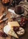 Glass of red wine with selection of various cheese on the board and grapes on wooden background. Blue Stilton, Red Leicester and Royalty Free Stock Photo