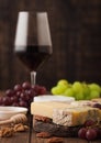 Glass of red wine with selection of various cheese on the board and grapes on wooden background. Blue Stilton, Red Leicester and Royalty Free Stock Photo