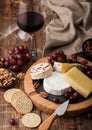 Glass of red wine with selection of various cheese on the board and grapes on wooden background. Blue Stilton, Red Leicester and