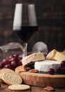 Glass of red wine with selection of various cheese on the board and grapes on wooden background. Blue Stilton, Red Leicester and Royalty Free Stock Photo