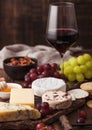 Glass of red wine with selection of various cheese on the board and grapes on wooden background. Blue Stilton, Red Leicester and Royalty Free Stock Photo