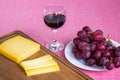 Glass of red wine, sliced yellow cheese Edam on brown wooden cutting board and sweet red grapes on white plate. Still life on a Royalty Free Stock Photo