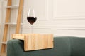 Glass of red wine on sofa with wooden armrest table in room, space for text. Interior element Royalty Free Stock Photo