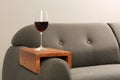 Glass of red wine on sofa with wooden armrest table in room, space for text. Interior element Royalty Free Stock Photo