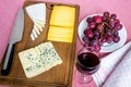 Glass of red wine, sweet red grapes on white plate and tree types of sliced cheese on brown wooden cutting board.