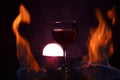 Glass of red wine on glass table with fire around it on black background, romantic photo