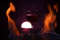 Glass of red wine on glass table with fire around it on black background, romantic photo Royalty Free Stock Photo