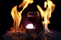 Glass of red wine on glass table with fire around it on black background, romantic photo Royalty Free Stock Photo