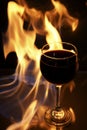 Glass of red wine on glass table with fire around it on black background, romantic photo Royalty Free Stock Photo
