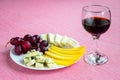 Glass of red wine and tree kinds of sliced cheese and sweet red grapes on white plate. Cheeses covered with edible white and blue Royalty Free Stock Photo