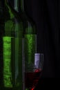A glass of red wine between two green wine bottles on a black background, isolated Royalty Free Stock Photo