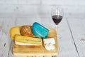 Glass of red wine and variation of cheese on wooden board.