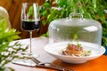 Glass of red wine and veal medallion with vegetables under transparent cap. Restaurant serving Royalty Free Stock Photo