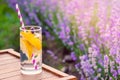 A glass of refreshing lemonade over a wooden chair. Blooming lavender flowers in the background.