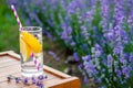 A glass of refreshing lemonade over a wooden chair. Blooming lavender flowers in the background.