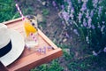 A glass of refreshing lemonade and a straw hat over a wooden chair. Blooming lavender flowers in the background.