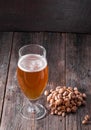 A glass of refreshing light beer and a scattered handful of pistachios on a table of old textured wooden boards.