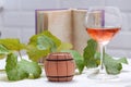 Glass with rose wine and a wooden barrel with a branch and leaves of grapes and a book on a white wooden table. Royalty Free Stock Photo