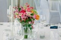 Glass round vase with bright bouquet of flowers on a table set up for dinner.