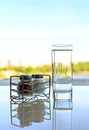 Glass salt and pepper shakers with glass of water on white table with reflection and summer background