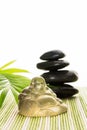 Glass smiling Buddha with stones and leaves on bamboo mat, isolated on white background. Royalty Free Stock Photo