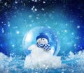 Glass snow globe with snowman on blue snowing Christmas background.