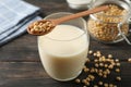 Glass of soy milk, soybeans seeds on spoon, napkin on wooden background, space for text