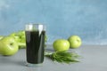 Glass of spirulina drink, wheat grass and apples on table against color background.