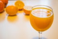 A glass of squeezed orange juice closeup, fresh and juicy oranges and lemon on a bright yellow and white background.. Royalty Free Stock Photo