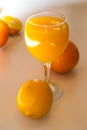 A glass of squeezed orange juice closeup, fresh and juicy oranges and lemon on a bright yellow and white background.. Royalty Free Stock Photo