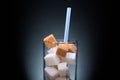 Glass with straw full of sugar and cubes on black background