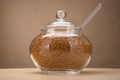 Glass sugar bowl with brown sugar on cardboard background