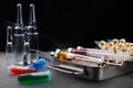 Syringes with medication on sterilization box, ampoules and vials with fluid on mist-covered surface