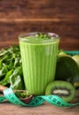 Glass of tasty green smoothie with ingredients and measuring tape on wooden table. Diet concept