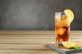 Glass of tasty ice tea with lemon on wooden table against grey background Royalty Free Stock Photo