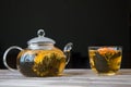 A glass tea pot with Flower Chinese tea and a cap of green tea on wooden table in front of dark background Royalty Free Stock Photo