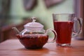 A glass teapot filled with hot fruit tea flavored with apple and spice with a served glass and blur background