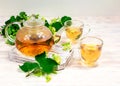 A glass teapot and two cups of tea with a linden tree on a wooden table against a background of linden leaves and Royalty Free Stock Photo