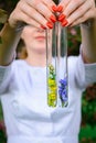 Glass test tubes with flower samples, close-up. Female hands holding flasks, blurred background. Study of plants, medicinal herbs