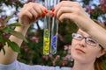 Glass test tubes with flower samples, close-up. Female hands holding flasks, blurred background. Study of plants, medicinal herbs