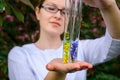 Glass test tubes with flower samples, close-up. Female hands holding flasks, blurred background. Study of plants, medicinal herbs