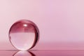 Glass transparent ball on light pink background and mirror surface.