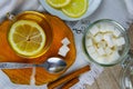 Glass transparent cup with mint tea stands on a wooden stand, next to a sugar bowl with sugar cubes, sliced lemon and a spoon