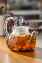 Glass transparent kettle with hot apple tea on wooden table at cafe