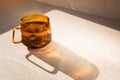 Glass transparent orange mug with hot green tea, shadow and reflection on light stone background