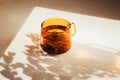 Glass transparent orange mug with hot green tea, shadow and reflection on light stone background