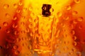 Glass transparent rectangular perfume bottle on a golden background with a silhouette of stalks. Close up water drops on