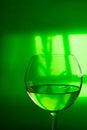 Glass of transparent white dry wine on green translucent background with window reflexion hard shadows. Conceptual creative